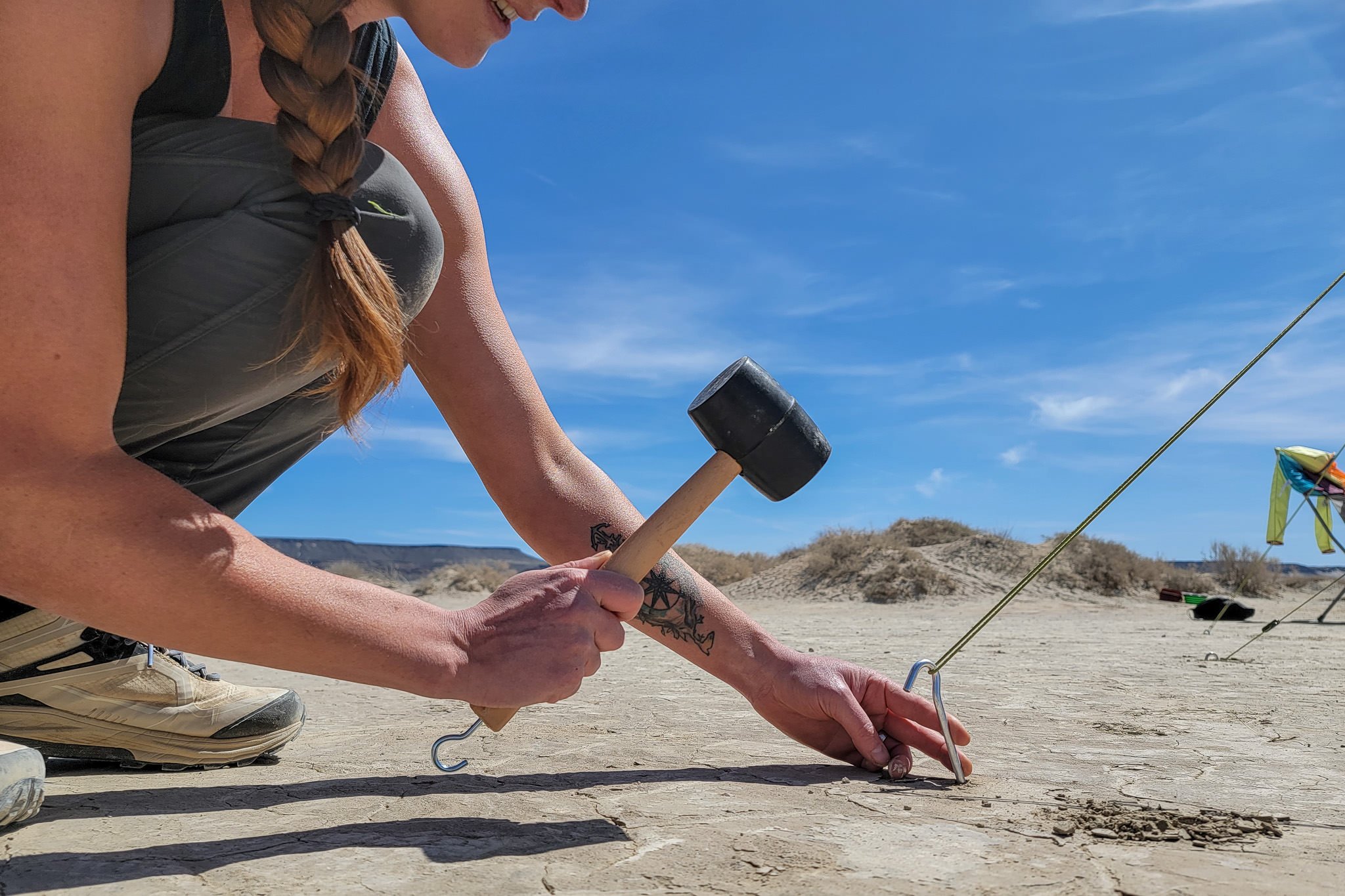 A person pounding a tent stake into the ground with the Coleman Rubber Mallet