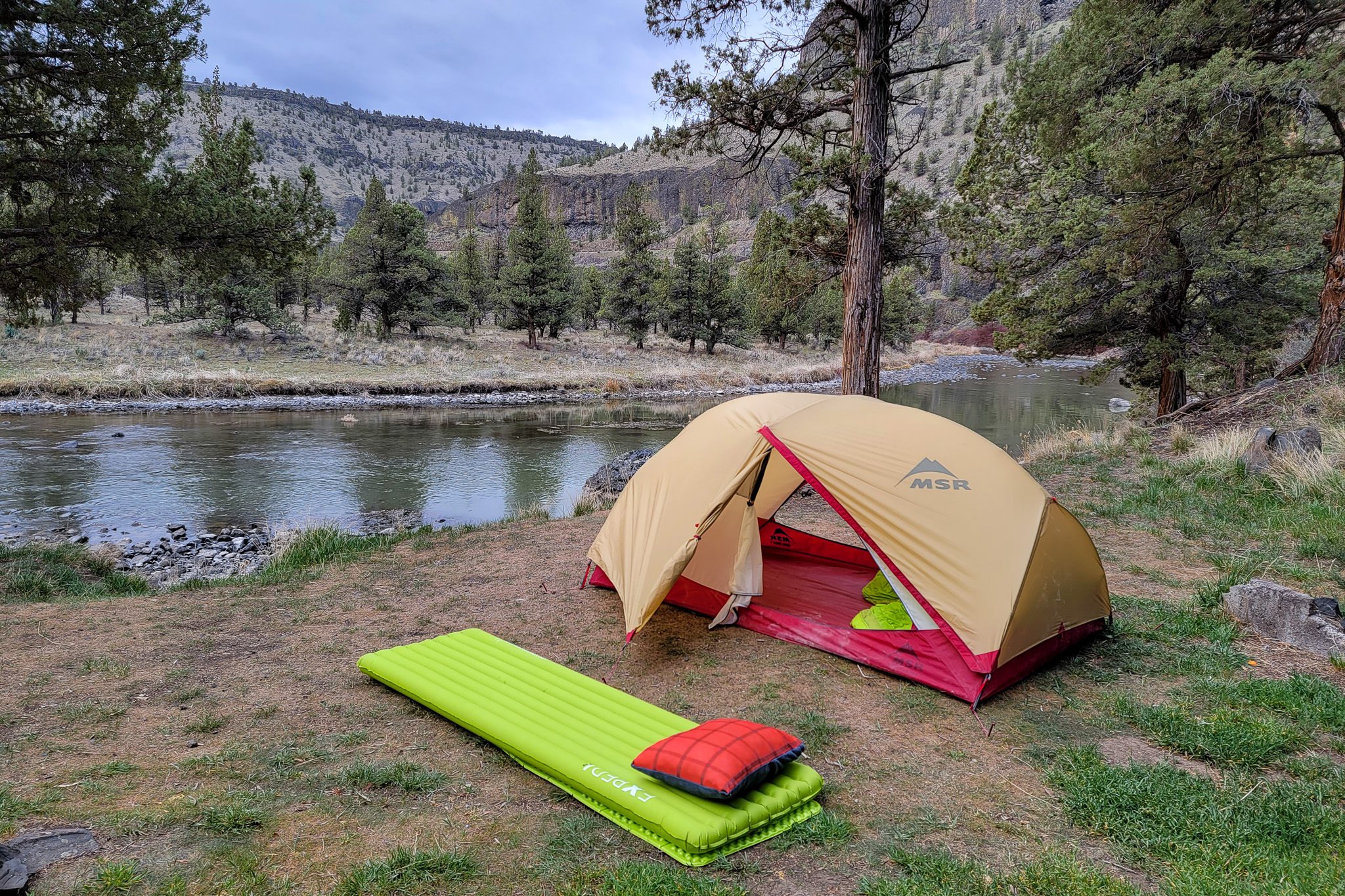 A backpacking sleeping pad outside of a tent by the river