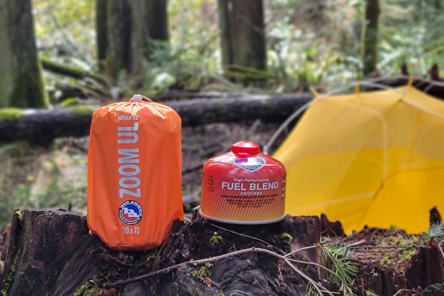 The Big Agnes Zoom UL packed in a stuff sack sitting next to a fuel canister with a tent in the background