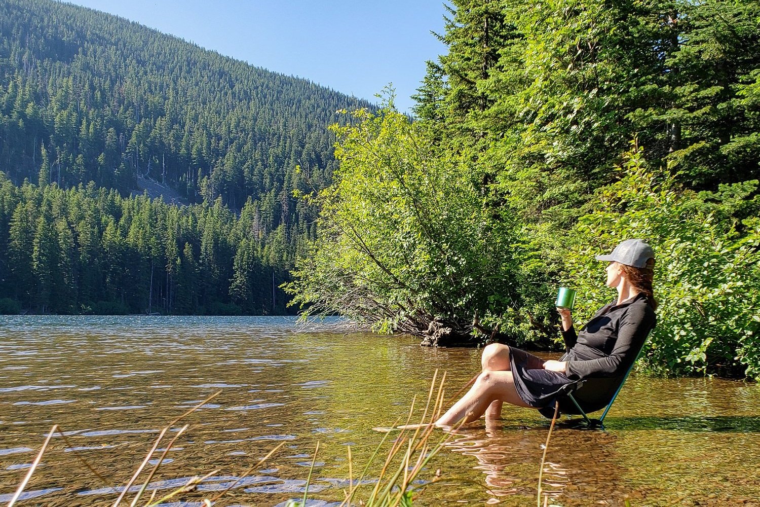 A backpacker relaxing in the shallow water on a lakeshore in the Helinox Chair Zero