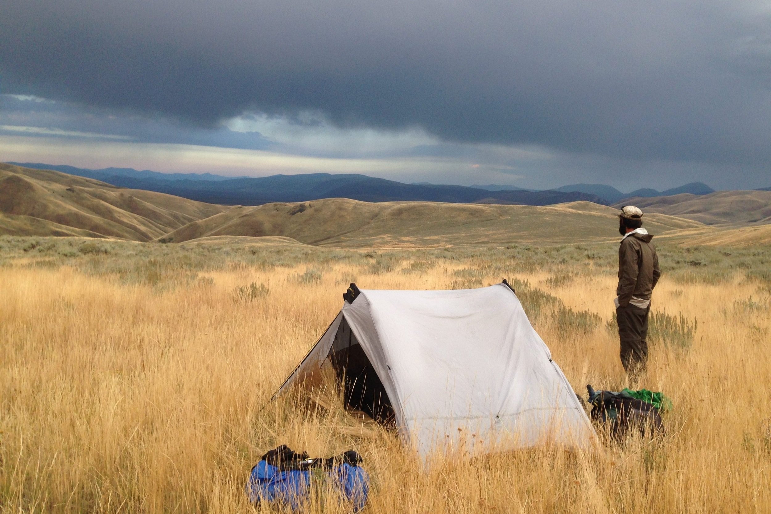 A backpacker standing next to the Six Moon Designs Lunar Duo in some foothills on the Continental Divide Trail