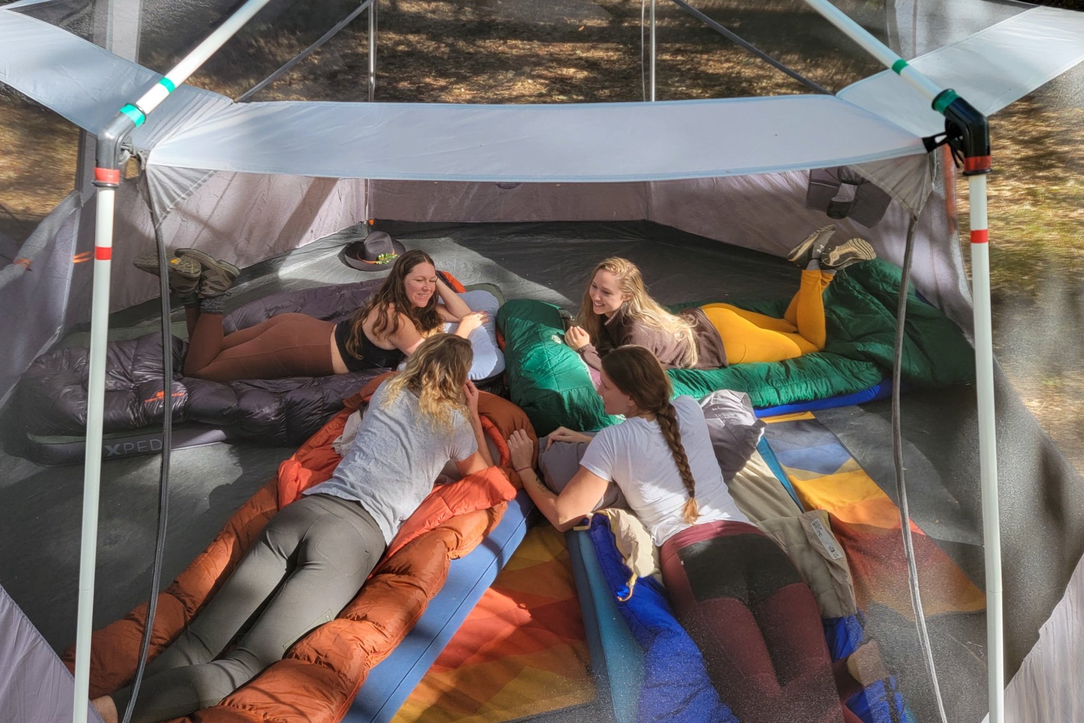 A group of women laying on sleeping bags in a  large camping tent