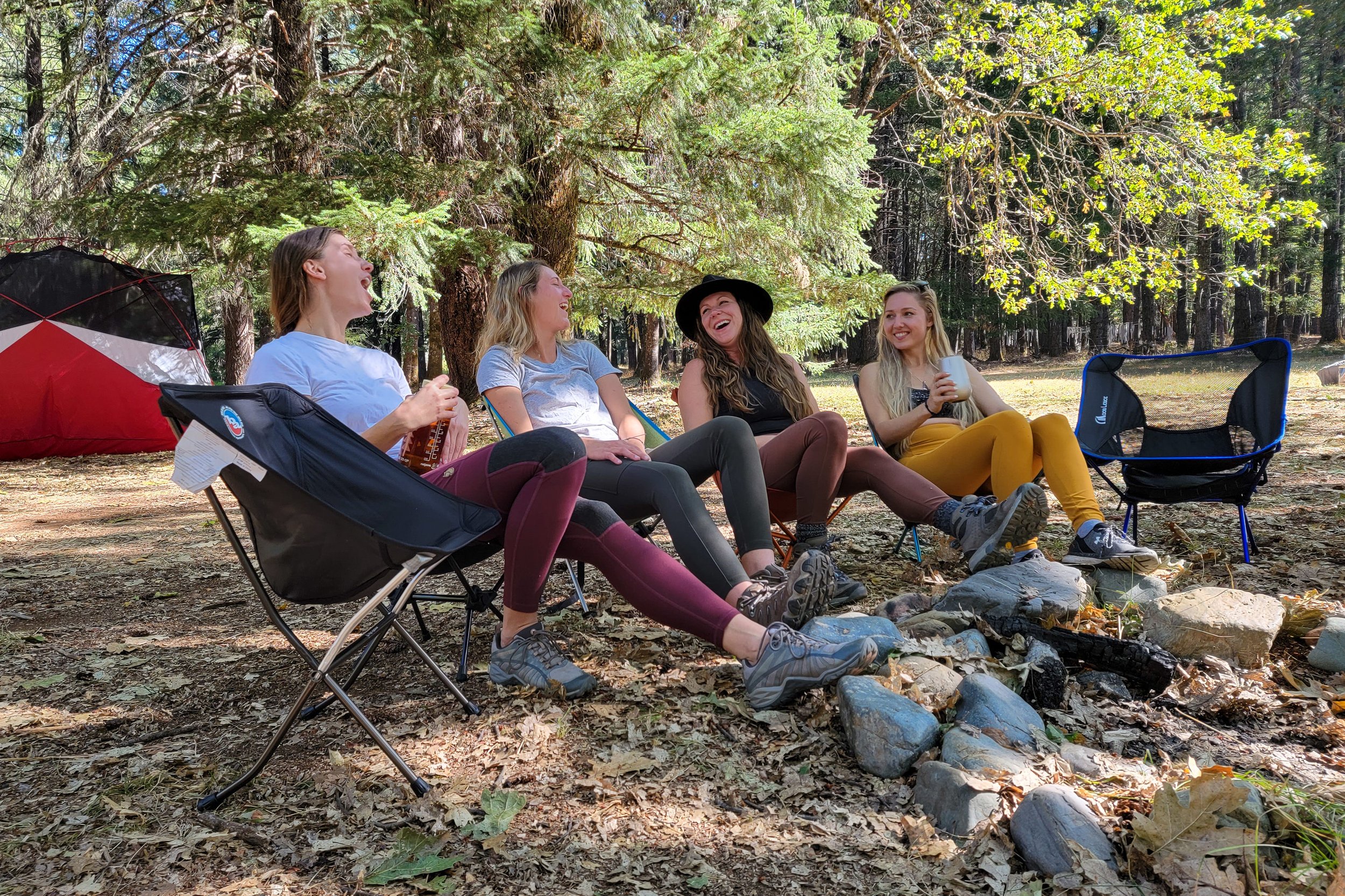 Four people sitting in camp chairs around a campfire