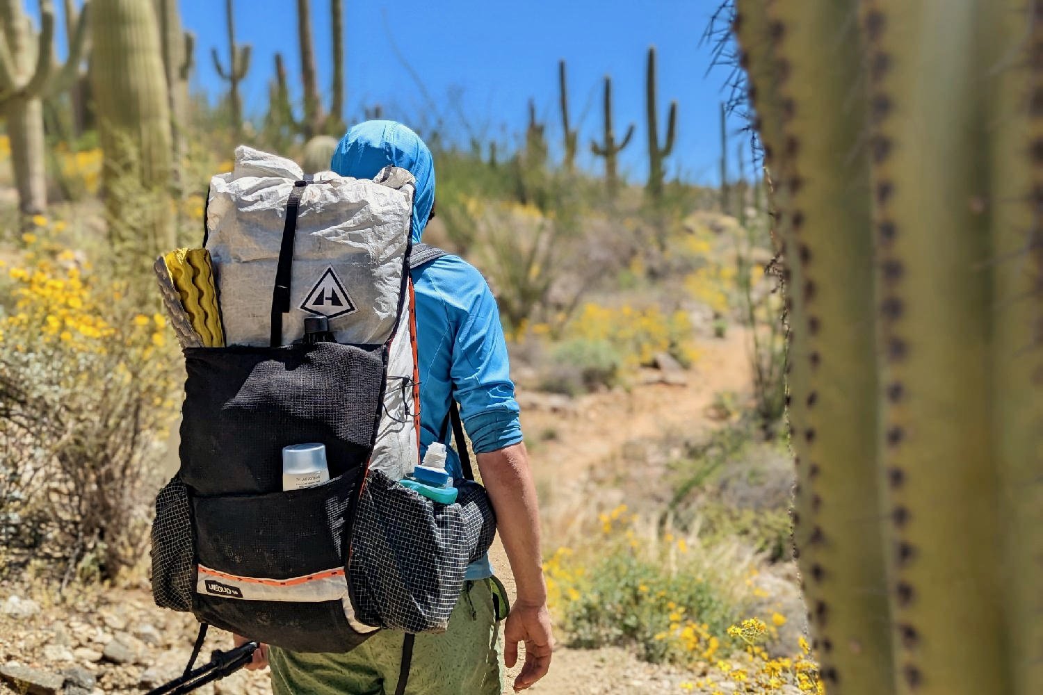 A hiker wearing the Hyperlite Mountain Gear Unbound 40 backpack on a trail in Saguaro National park - there are blurred saguaro cacti in the foreground and background