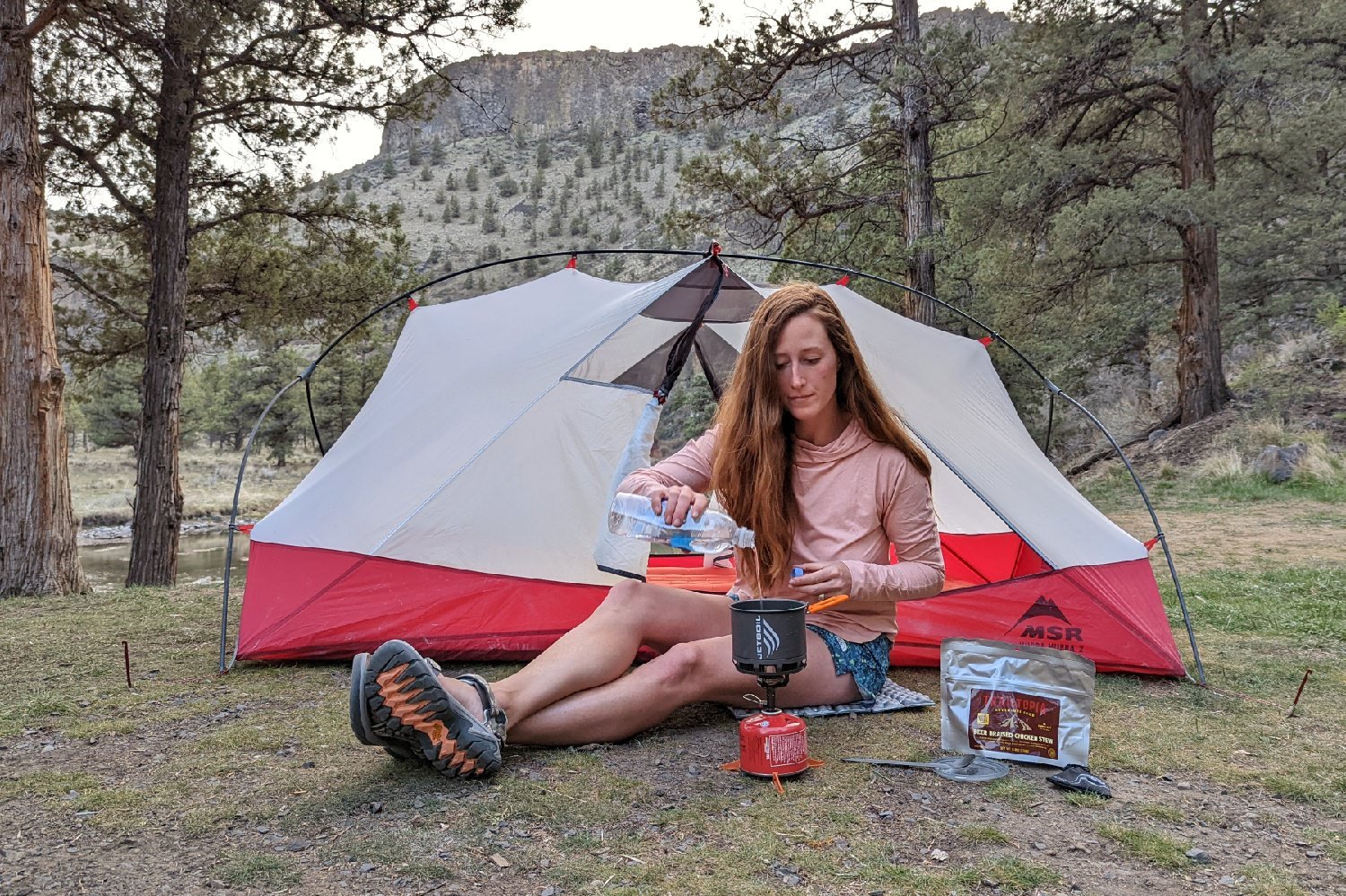 A woman wearing the REI Trailmade shorts and pouring water into a cookpot in front of a backpacking tent