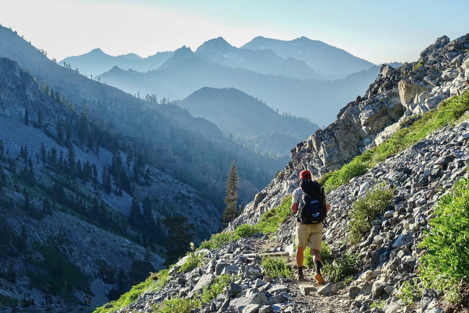 A backpacker wearing the ULA circuit hiking in the mountains with many distant peaks in the background