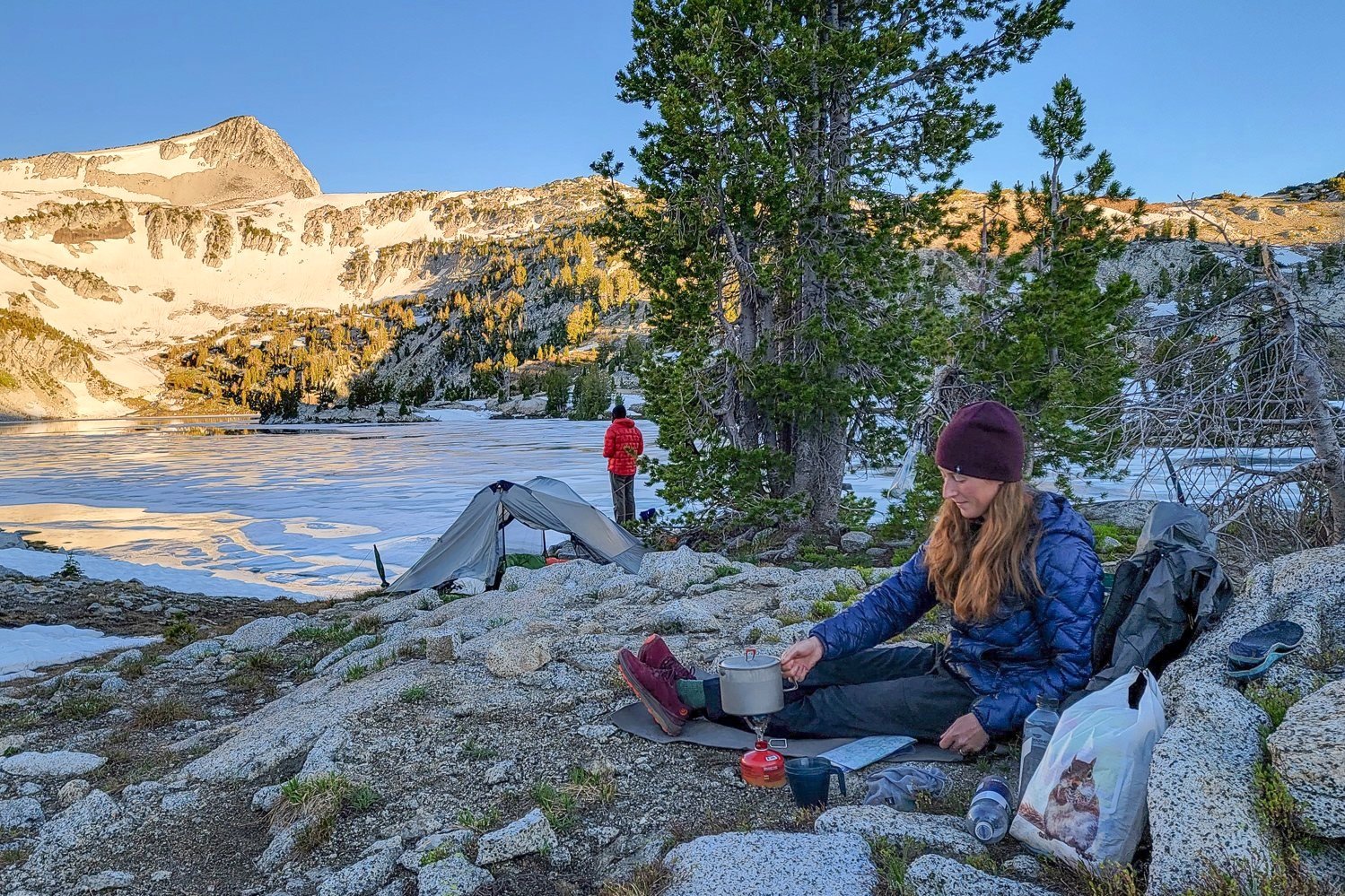 A backpacker using the Gossamer Gear Thinlight Pad as a seat while cooking in camp