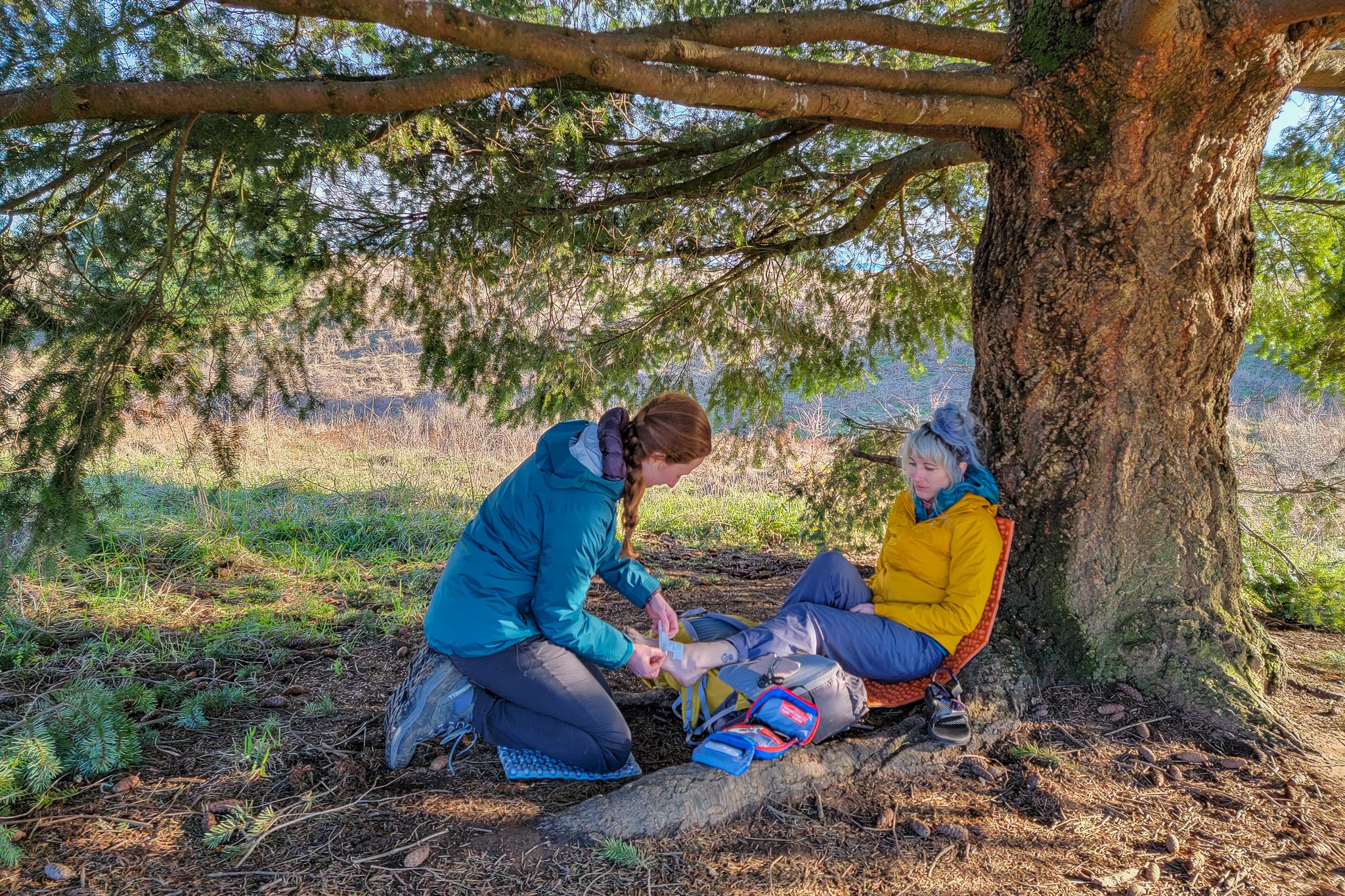 A hiker using supplies from the AMK Hiker First Aid Kit to patch up a wound on a fellow hiker