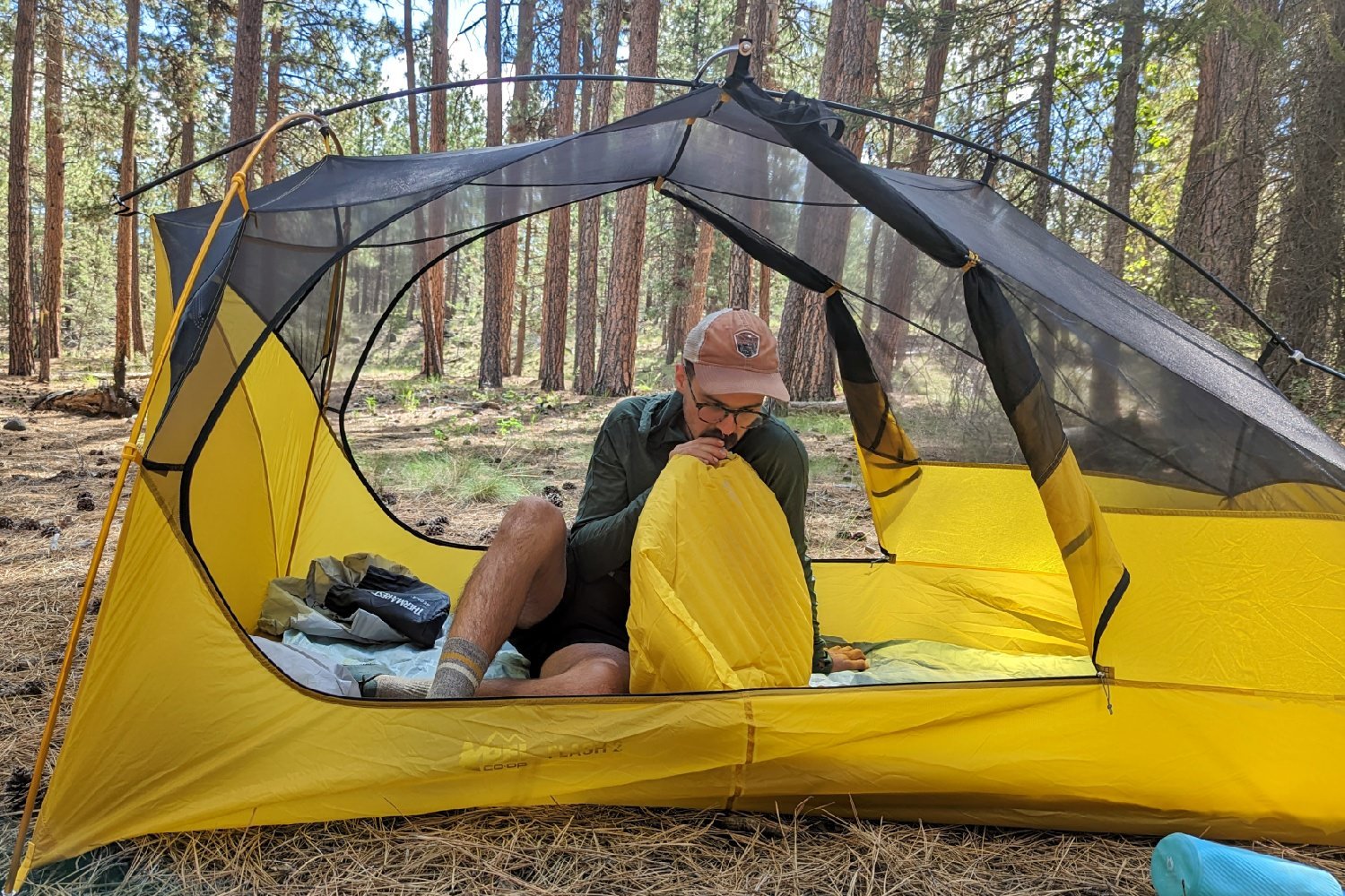 A hiker sitting inside the REI Flash 2 Tent blowing up an air pad - both doors of the tent are open