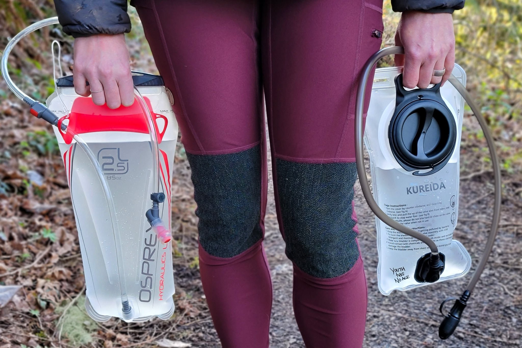 Closeup of a hiker holding the Osprey Hydraulics and Kureida hydration bladders by her knees.