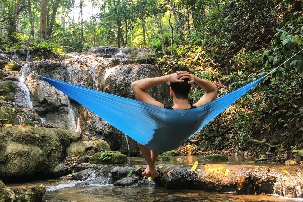 A hiker relaxing in front of a waterfall in the Hummingbird Single Hammock