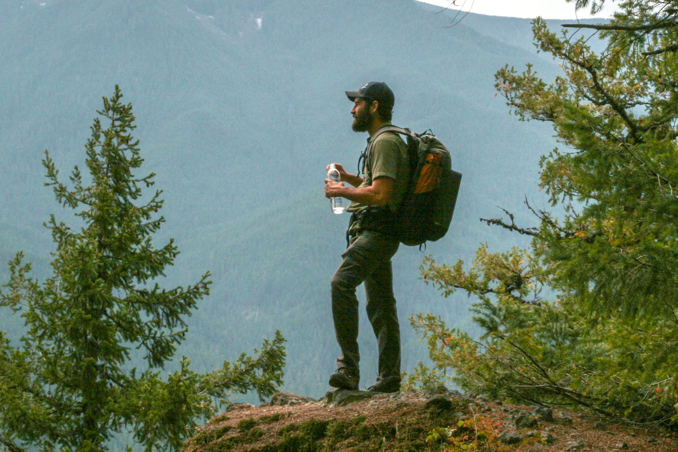 A hiker holding a Smartwater bottle standing in front of a mountain view