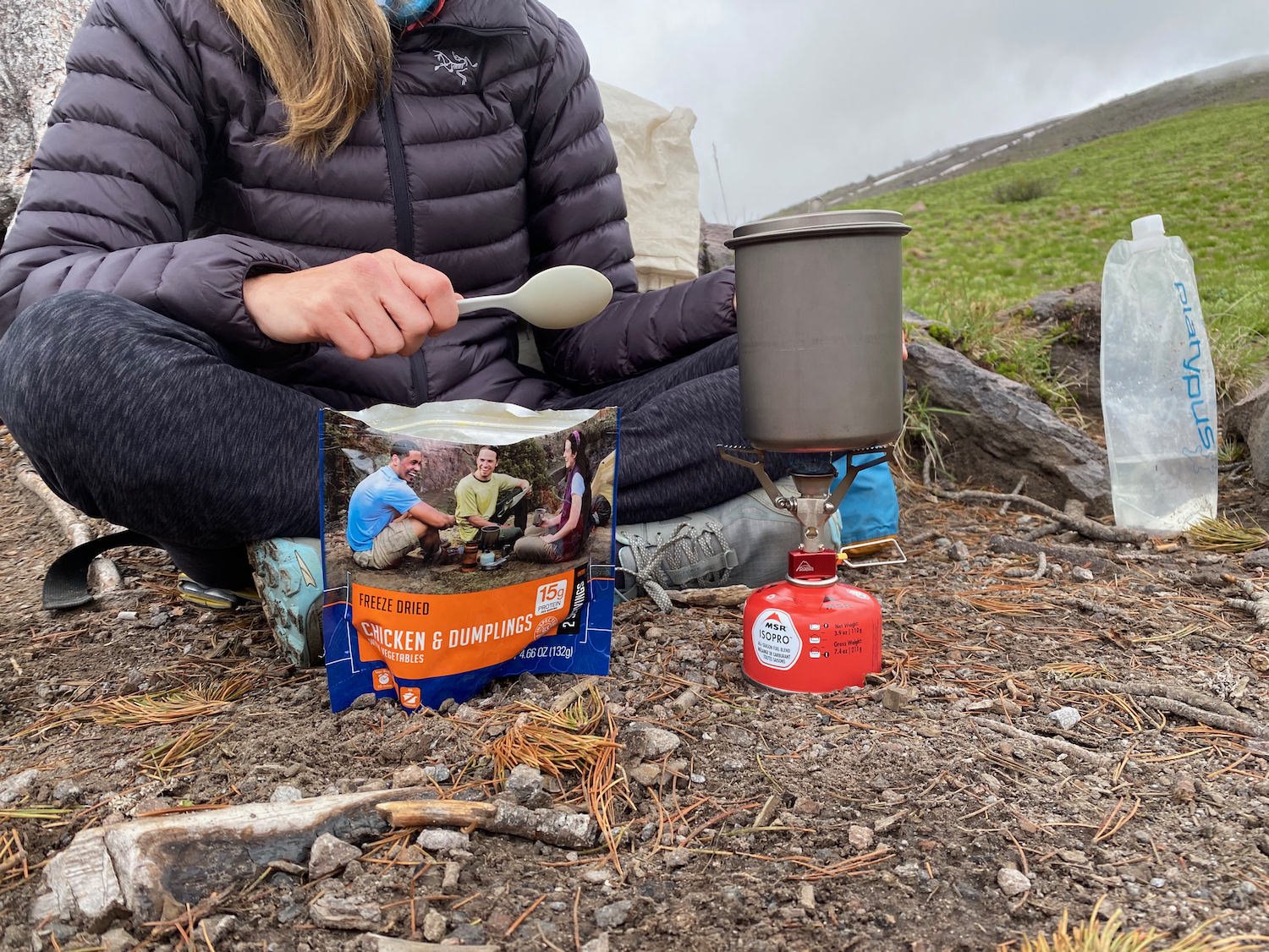 A hiker surrounded by backpacking cookware and a freeze dried meal from Mountain House