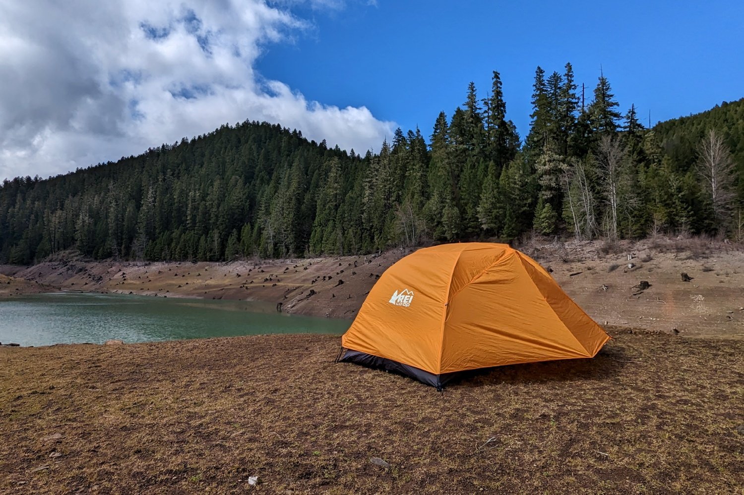 The REI Half Dome SL 2 Plus set up in front of a lake with some mountains in the background