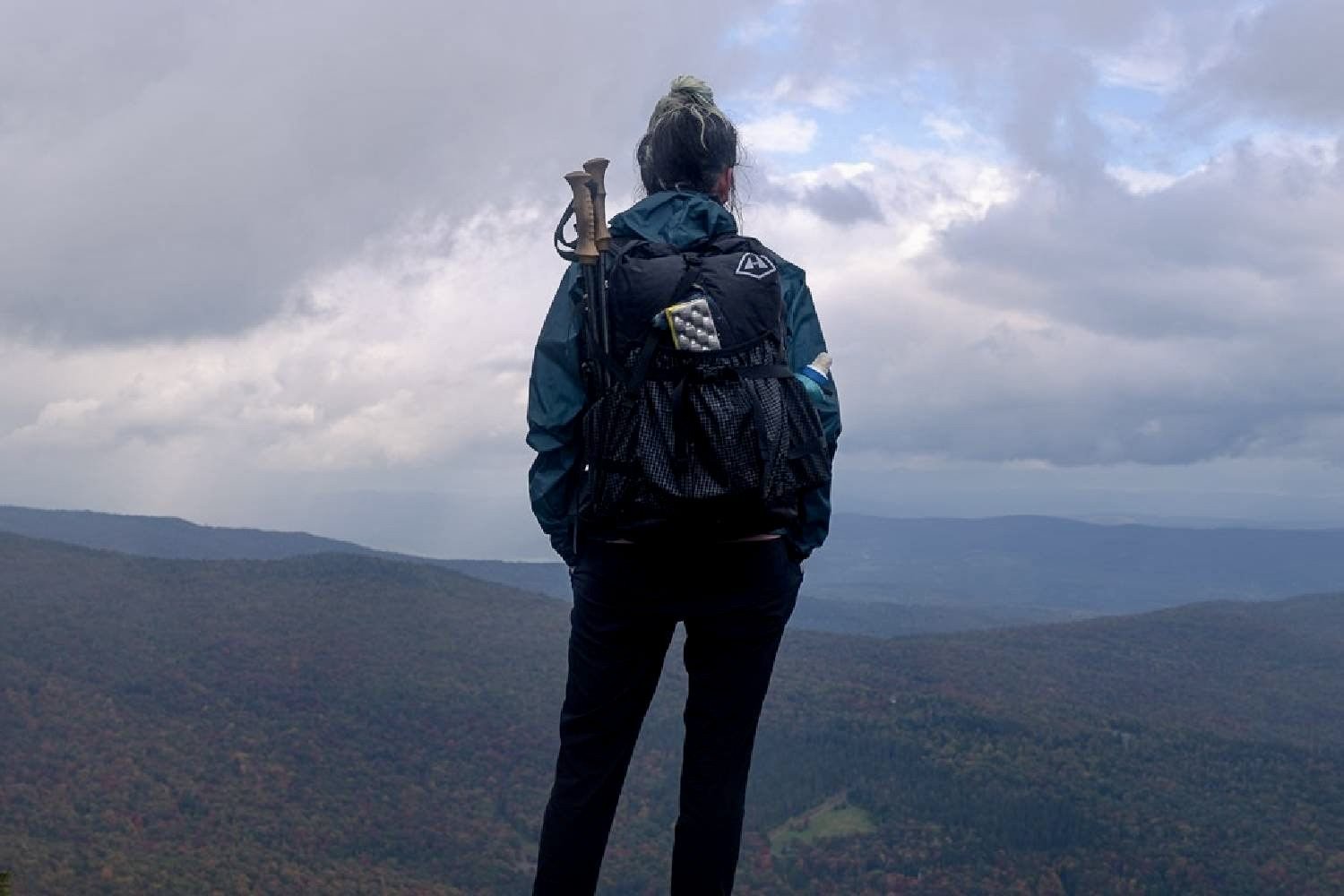 A hiker wearing the Hyperlite Mountain Gear Southwest 2400 standing on a ledge looking at a cloudy mountain view