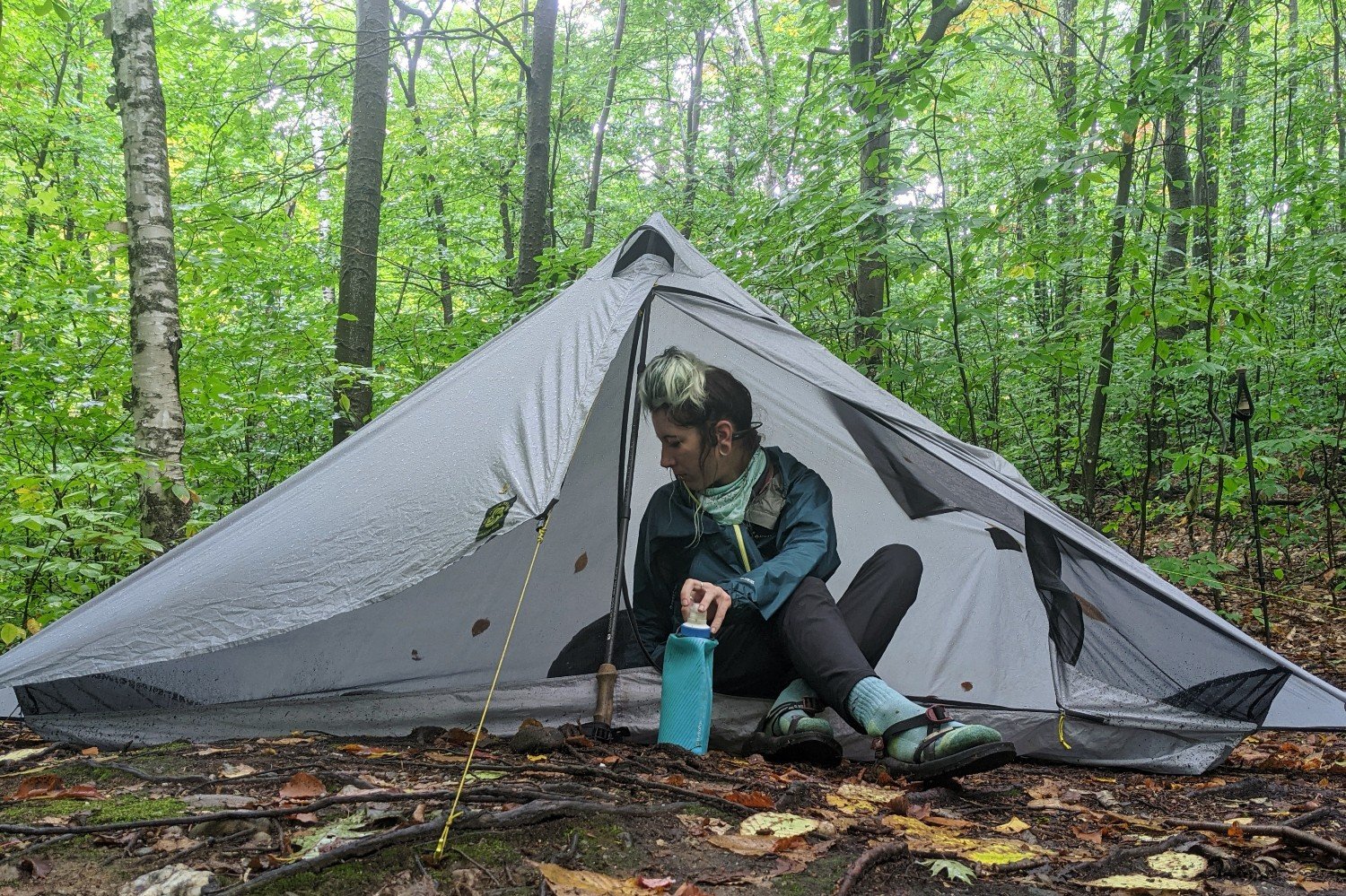 A hiker sitting inside the Six Moon Designs Lunar Solo set up in a forest