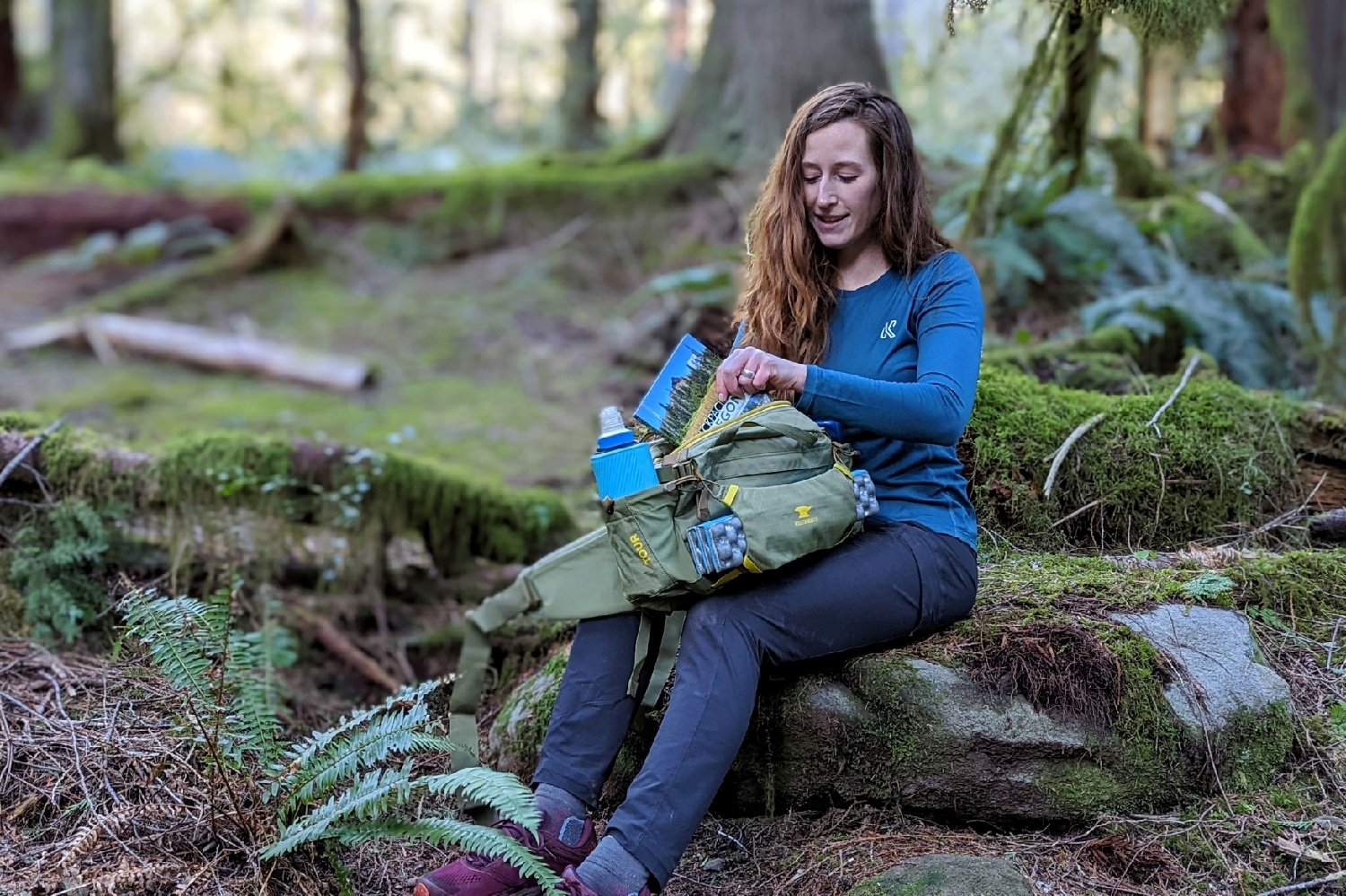 A hiker sitting on a rock pulling a hiking guidebook out of the Mountainsmith Tour fanny pack