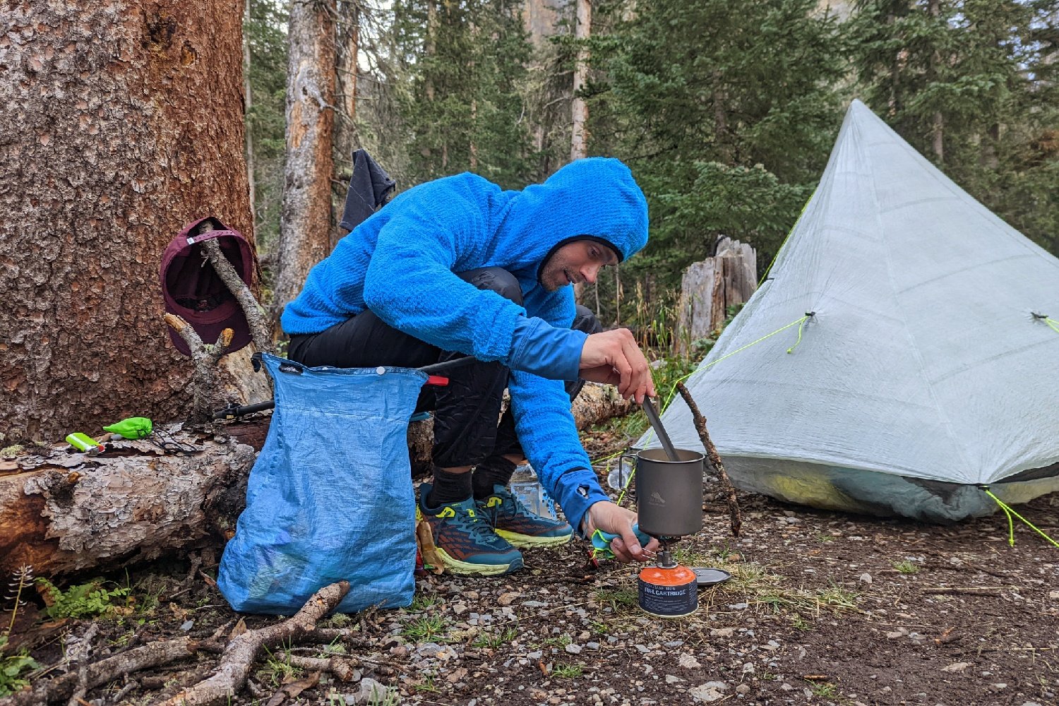 A hiker cooking at a campsite with a Hilltop Packs Food Bag next to them