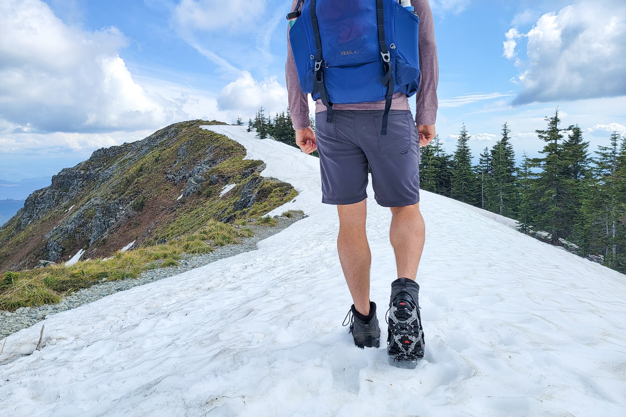 A hiker walking up a snowfield on a mountain in Prana Brion II shorts