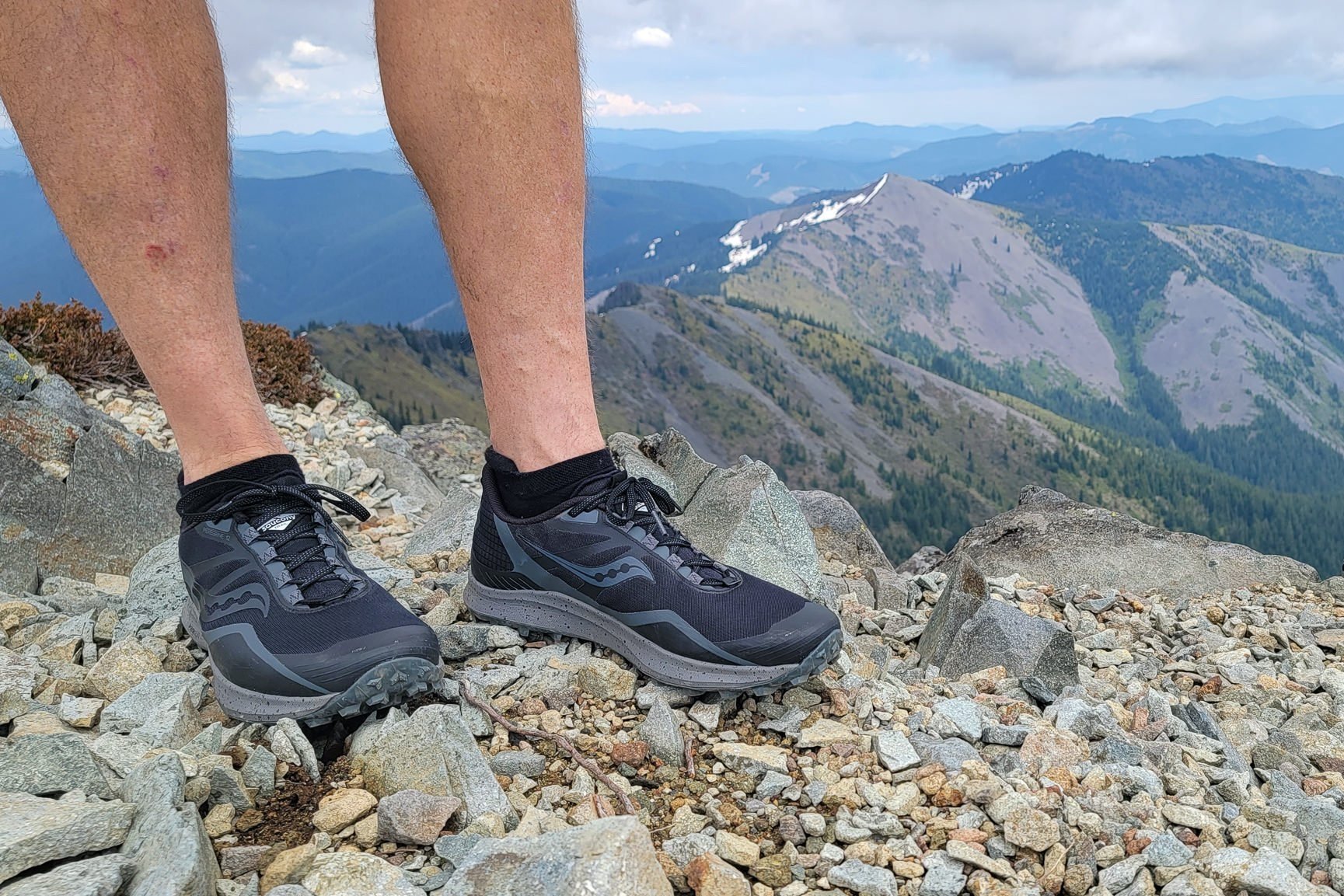 A shin down view of a hiker's legs and feet wearing Suacony Peregrines with a mountain ridgeline in the background