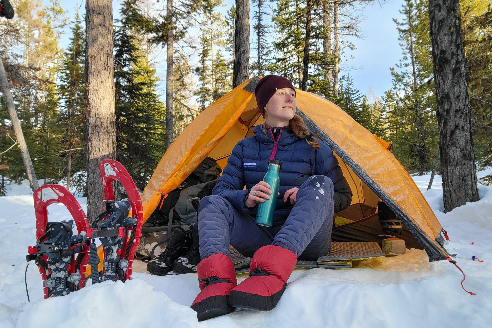 A woman wearing the Feathered Friends Down Booties in a snowy winter camp