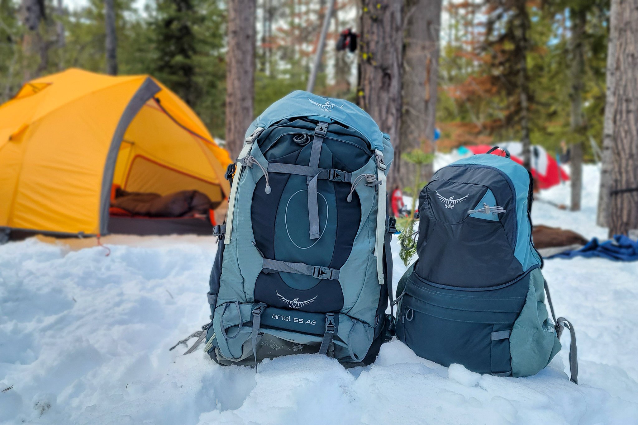 Osprey Ariel 70 backpack sitting in a snowy campsite next to the included daypack