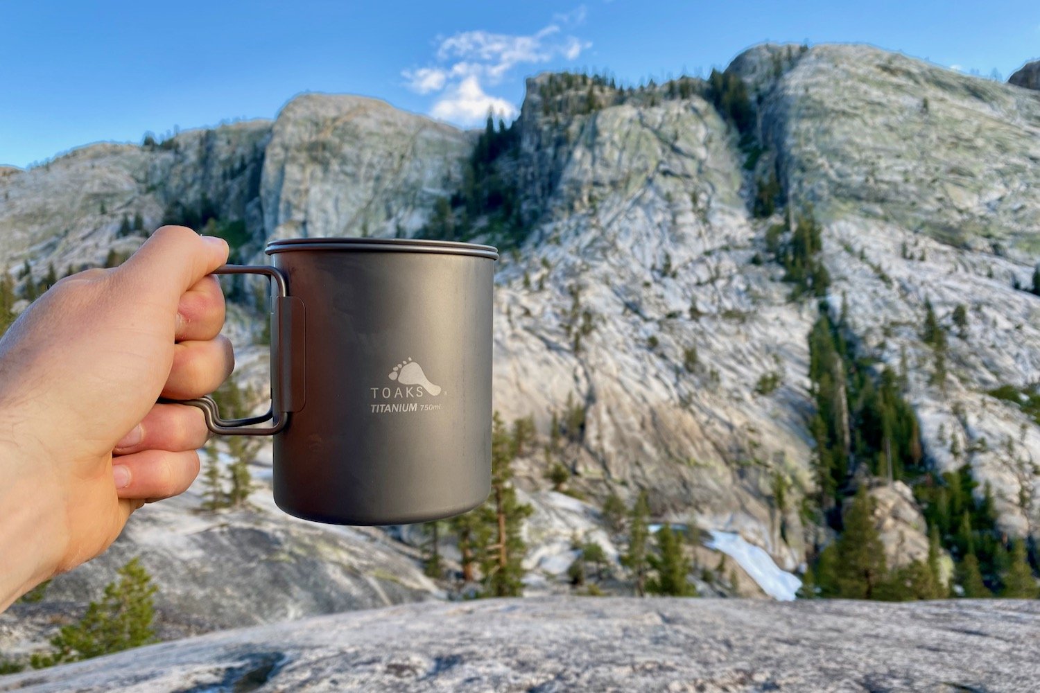 A backpacker holding a TOAKS Titanium Pot in front of a granite peak